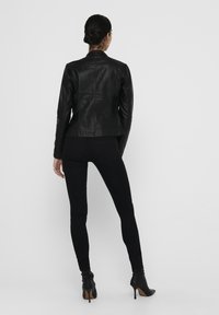 Black leather jacket with a fitted design, high collar, and subtle stitching details, paired with black skinny jeans and heeled ankle boots.