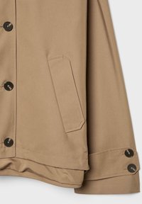 Beige jakkeafsnit, der viser sidelomme, knappet front og ærme med dobbelt knappet manchet på hvid baggrund.