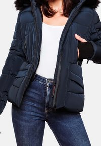 Granatowa kurtka puchowa z kapturem wykończonym futrem, z zamkiem błyskawicznym z przodu i ściągaczami przy mankietach. Posiada wyściełane sekcje oraz kieszenie z przodu.