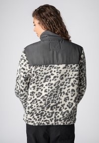 Faux fur jacket featuring a leopard print in black and white, with a contrasting gray shoulder panel and high collar. Textured, warm design.