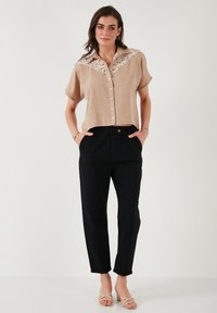 Chemise en lin beige à boutons avec un col agrémenté de dentelle, associée à un pantalon noir cintré et des escarpins crème à lanières.