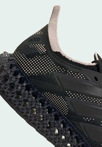 Gros plan d'une basket noire et beige avec une tige en maille texturée, un motif à pois et une semelle translucide à structure en treillis.