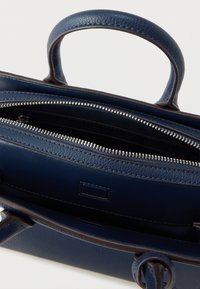 Granatowa skórzana torba na ramię o usztywnionej konstrukcji, z górnymi uchwytami, zamknięciem na zamek błyskawiczny oraz wewnętrznymi przegródkami do organizacji.