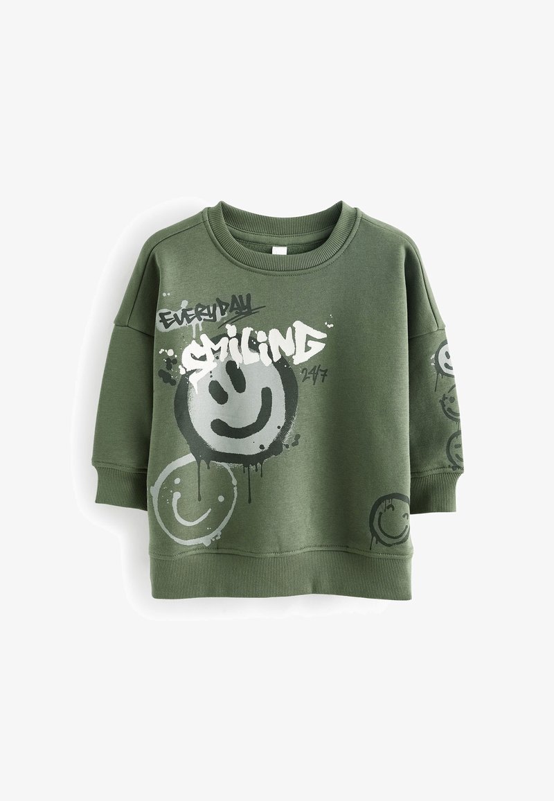 Sweat-shirt vert olive avec poignets et ourlet côtelés, arborant de grands et petits visages souriants peints ainsi que le texte "EVERYDAY SMILING 24/7" sur le devant et la manche.