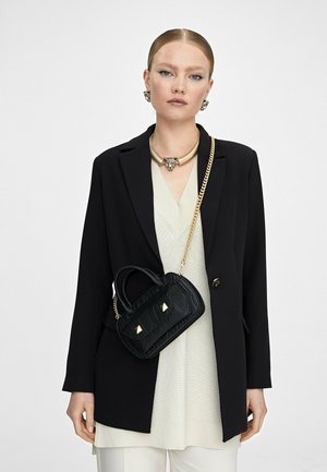 Bolso de mano de textura de cocodrilo negro con acentos de hardware dorado. Usado como bandolera con una correa de cadena, cuenta con asas cortas y una forma rectangular.