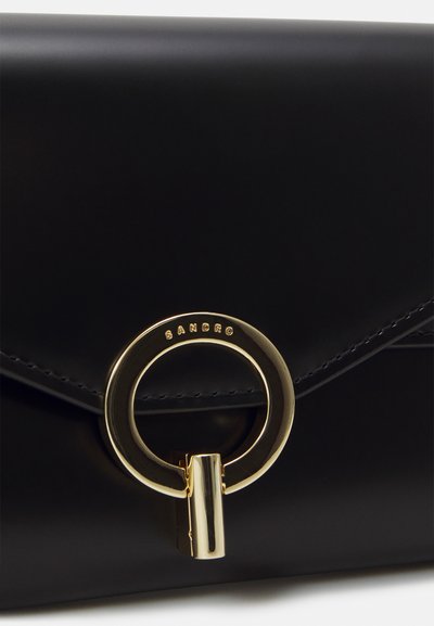 Borsa a tracolla in pelle nera con chiusura a patta, hardware circolare dorato e logo del marchio impresso. Texture liscia con dettagli di cucitura raffinati.