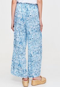 Szerokie spodnie w jasnoniebieskim kolorze z kwiecistym wzorem. Widok z tyłu pokazuje elastyczny pas i luźny krój, zestawione z sandałami na koturnie.