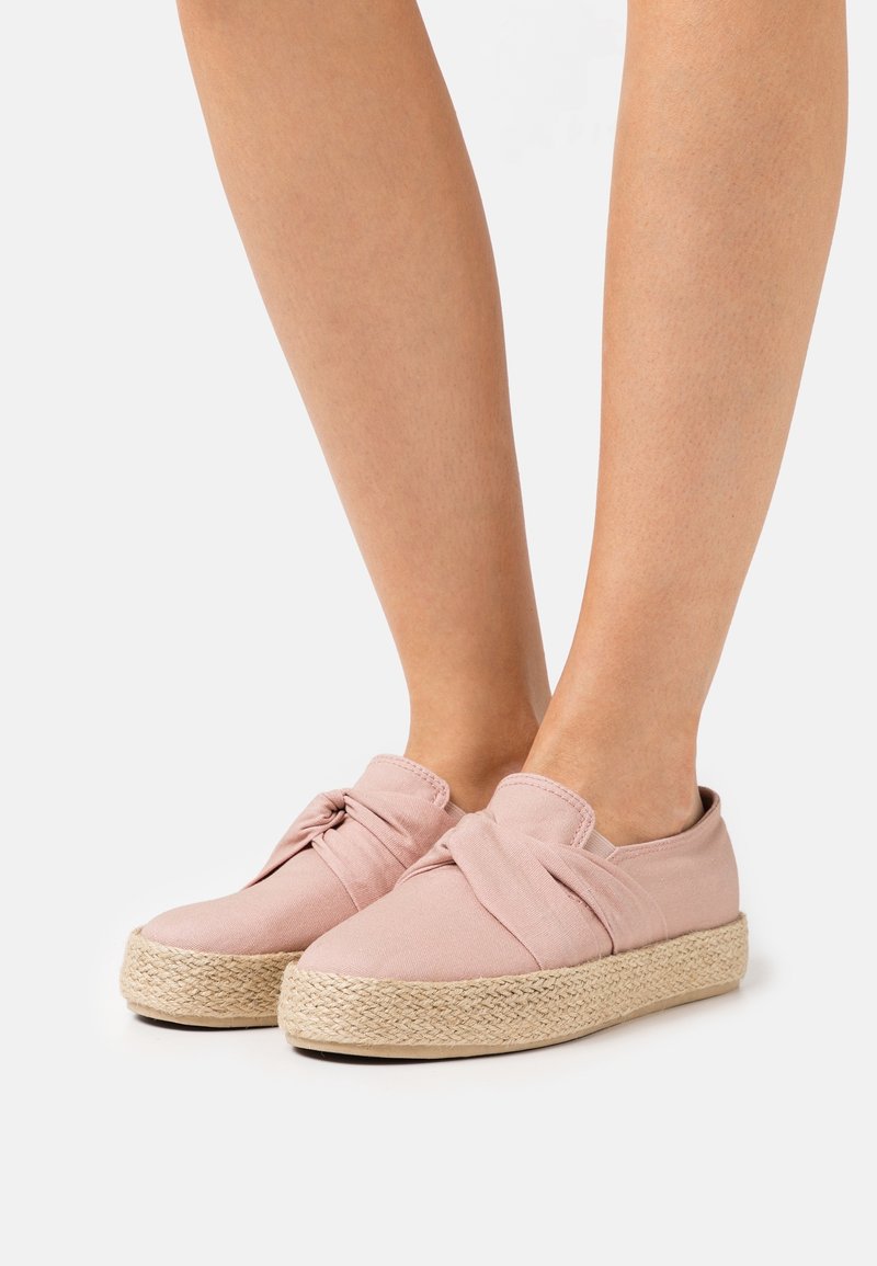 Espadrilles en toile rose avec un design noué, dotées d'une semelle en corde de jute. La texture est lisse et la forme est un style à enfiler arrondi.