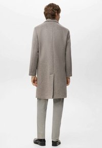 Grijze wollen jas met een getailleerde pasvorm, enkele split en ingezette kraag, gecombineerd met lichtgrijze broek en zwarte schoenen.