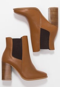 Stivali tronchetti in pelle marrone con un pannello laterale elastico nero e un tacco in legno strutturato. Design a punta. Finitura liscia.
