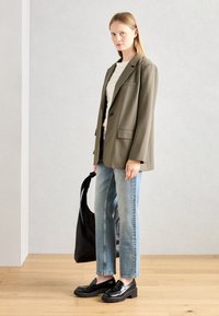 Olive green oversize blazer, biały teksturowany sweter, jasnoniebieskie jeansy o prostym kroju, czarne loafersy na платформie i czarna torba na ramię.