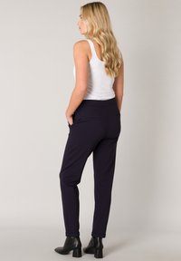 Marineblauwe tapered broek met een elastische tailleband en zakken, gecombineerd met een aansluitend wit tanktop en zwarte enkellaarsjes. Gladde stoftextuur.