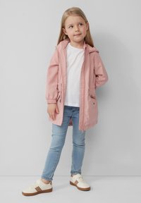 Różowa, lekka kurtka z kapturem, zapinana na zamek, z elastycznymi mankietami i kieszeniami, w połączeniu z białym t-shirtem, niebieskimi dżinsami i kremowymi trampkami z brązowymi akcentami.