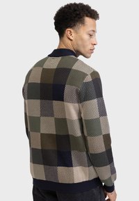 Veste en maille avec un design coloré composé de carrés verts, bleu marine et beiges, ainsi que de rayures diagonales ; finition avec un col et un ourlet en ribbed bleu marine.