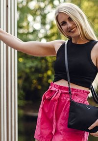 Černý žebrovaný top na ramínka a růžové šortky s vysokým pasem a zavázaným pasem. Na rameni je malá černá křížová taška.