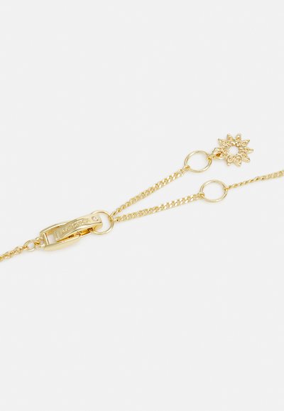 Bracelet en chaîne dorée avec un fermoir sécurisé, ornée d'un pendentif en forme de soleil et d'accents circulaires le long de la chaîne. Texture lisse et finition brillante.
