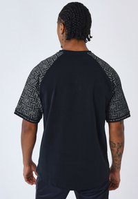 Camiseta negra con mangas cortas estampadas, que presenta diseños intrincados en blanco. Tejido suave con un corte relajado y cuello redondo.