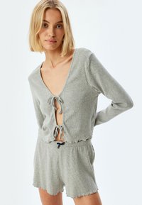 Gråt strikket loungewear sæt, der inkluderer en cropped top med dyb V-udskæring og bindelukning, der er parret med shorts med bølgede kanter.