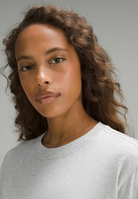 Szary bawełniany sweter z okrągłym dekoltem, luźnym krojem i miękką teksturą, noszony przez osobę z kręconymi włosami.