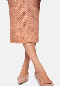 Knielanger, gestrickter Rock in glänzendem Roségold mit offenem Diamantmuster. Kombiniert mit rosa Wildleder-Ballerinas mit Schleifendetail.