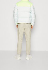 Jasnoniebieska kurtka puchowa z neonowozieloną górą, z wysokim kołnierzem i elastycznymi mankietami. W zestawie z jasnobeżowymi spodniami cargo i białymi trampkami.