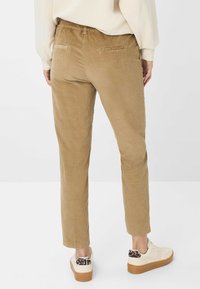 Pantalon en velours côtelé beige avec une ceinture élastique, coupe droite, deux poches arrière, associé à des baskets blanches avec un accent imprimé léopard.