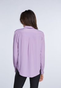 Camicia a maniche lunghe di un delicato color viola, con colletto, tessuto liscio, polsini bottonati e orlo curvo. Presenta un dettaglio a yoke sul retro.