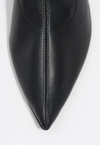 Czarny skórzany but w szpic, charakteryzujący się gładką teksturą, precyzyjnym przeszyciem wzdłuż szwu i elegancką sylwetką.