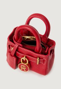 Väike punane tekstureeritud nahkotkott kahekordsete käepidemetega, kuldsete detailide ja esiosas asuva ümmarguse kuldse logo lukuga.