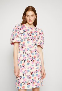 Vestido floral de manga curta com um fundo creme, padrões de flores rosas e azuis e ombros bufantes. Textura de tecido suave.