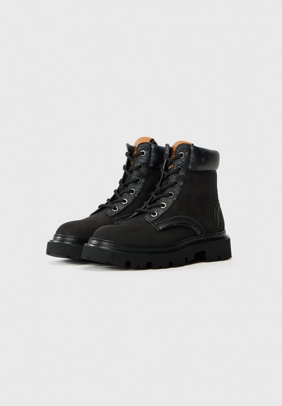 Bottes de cheville en suede noir avec une semelle robuste, présentant des accents en cuir contrastants et des œillets en métal pour les lacets. Col rembourré pour le confort.