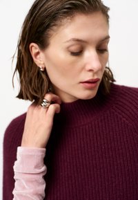 Bordeaux geribbelde trui met hoge hals, gelaagd over een lichtroze fluwelen lange mouw. Zilveren ringen en oorbellen voeden de metalen accenten.