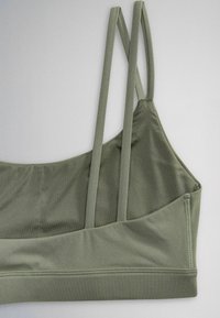 Olive green sports bra with double thin shoulder straps and smooth fabric, shown flat on a light gray surface.