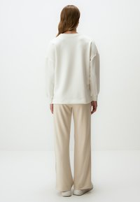 Witte pullover met lange mouwen en een ontspannen pasvorm, gecombineerd met beige, wijde broekspijpen. Soepele stofstructuur; minimalistisch ontwerp.