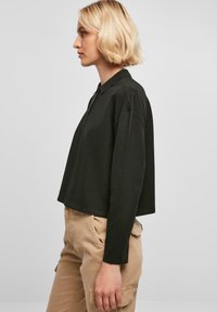 Mørkegrønn cropped genser med krage, lange ermer og en avslappet passform, vist på en modell mot en nøytral bakgrunn.