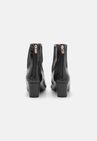 Botas negras hasta el tobillo hechas de cuero brillante, con dos cremalleras laterales, un tacón grueso y una textura suave.