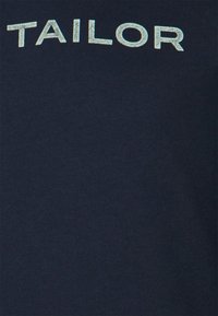 Mörkblå bomullströja med ordet "TAILOR" tryckt i en strukturerad, ljusblå färg över bröstet. Enkel och avslappnad design.