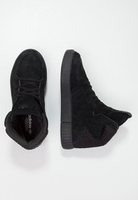 Černé vysoké tenisky s nubukovým svrškem a texturovanými detaily. Mají černou gumovou podrážku a polstrovaný límec pro podporu.