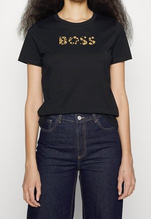 Woman wearing black short-sleeve T-shirt with gold leopard print "BOSS" text, paired with high-waisted dark blue jeans.
