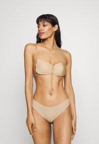 Haut bandeau nude sans bretelles avec des bords festonnés, design à lacer à l'avant, associé à un bas de bikini assorti à bords festonnés. Texture de tissu lisse.