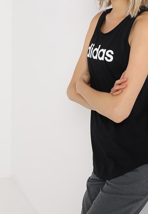 Canotta sportiva nera senza maniche con il logo bianco "adidas" sul petto; tessuto morbido e vestibilità rilassata, abbinata a pantaloni grigi.