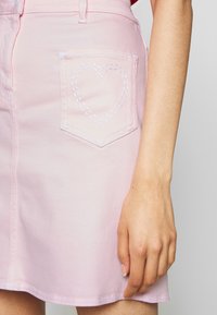 Vaaleanpunainen farkkuhame, jossa on takatasku, jossa on valkoista sydänkirjontaa, kapea vyötärö ja hieman levenevä helma.