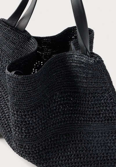 Μαύρη υφασμένη τσάντα ώμου με υφασμένο σχέδιο και δύο λείες δερμάτινες λαβές σε απλό φόντο.