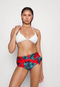 Top de biquíni triangular branco com tiras finas, combinado com um fundo de cintura alta vermelho com padrões de folhas tropicais verdes e um detalhe de laço.