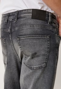 Ausgebleichte schwarze Jeans mit subtilen Waschungen, Fünf-Taschen-Design und einem glatten Bund mit mattem schwarzen Etikett.