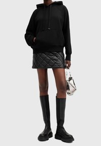 Black hooded sweatshirt with a front pocket, paired with a black quilted mini skirt and knee-high black leather boots. Silver bag accent.