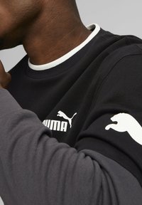 Czarna i szara bluza z białym prążkowanym kołnierzem, z wyraźnym białym logo Puma na piersi oraz białym logo na rękawie.