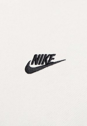 Witte textiel met een gestructureerd oppervlak, waarop een geborduurd zwart Nike-logo met een gebogen swoosh-design is te zien.