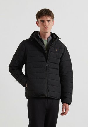 Veste rembourrée noire avec fermeture éclair, capuche réglable et texture matelassée. Dotée d'un accent de logo sur la poitrine. Associée à un pantalon sombre.