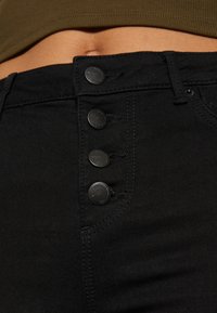 Høyt liv svarte jeans med fem-knapp lukking, med jevn tekstur og sydd detaljer langs sømmene.